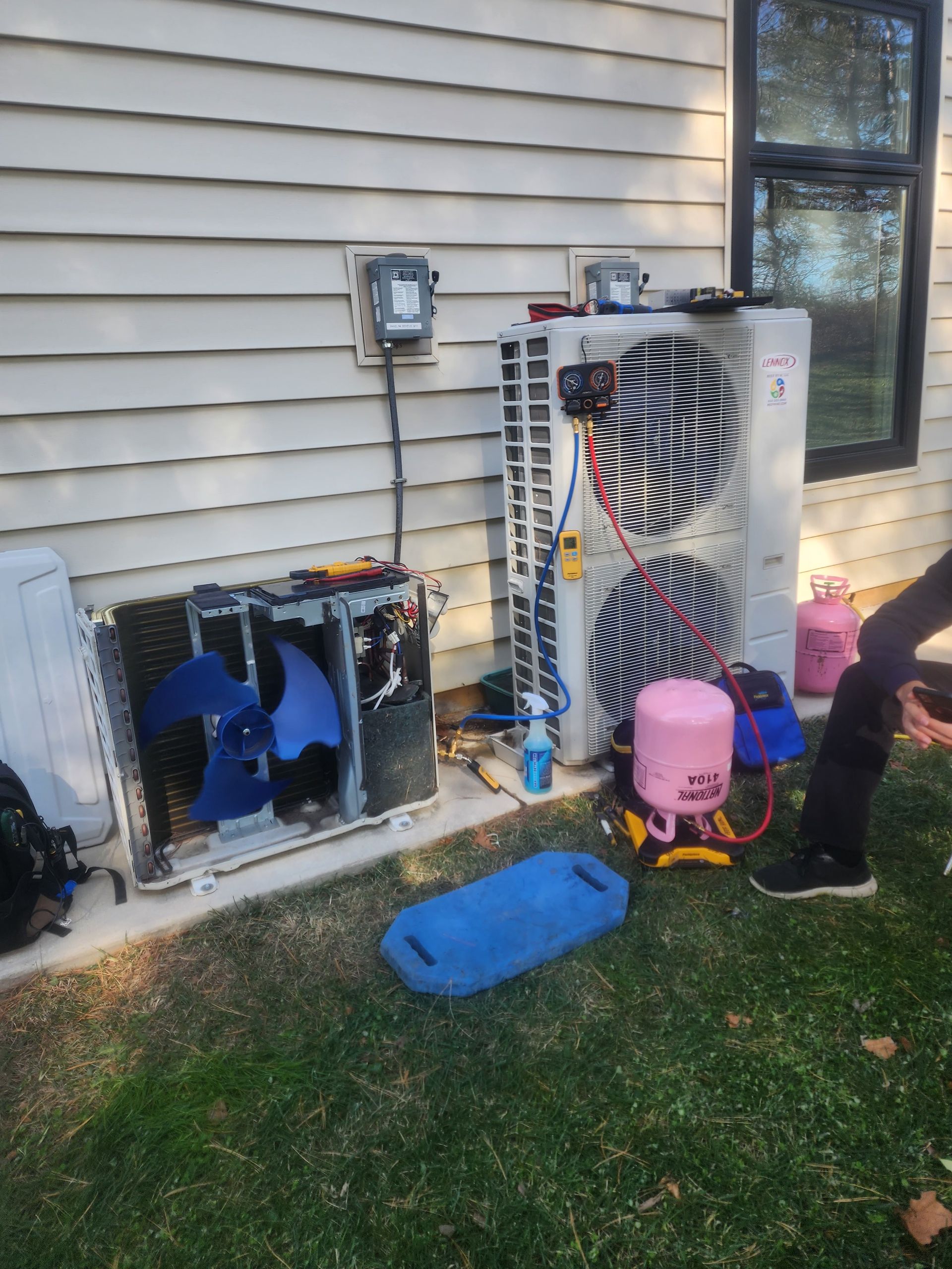 A man is sitting on the grass next to a broken air conditioner.