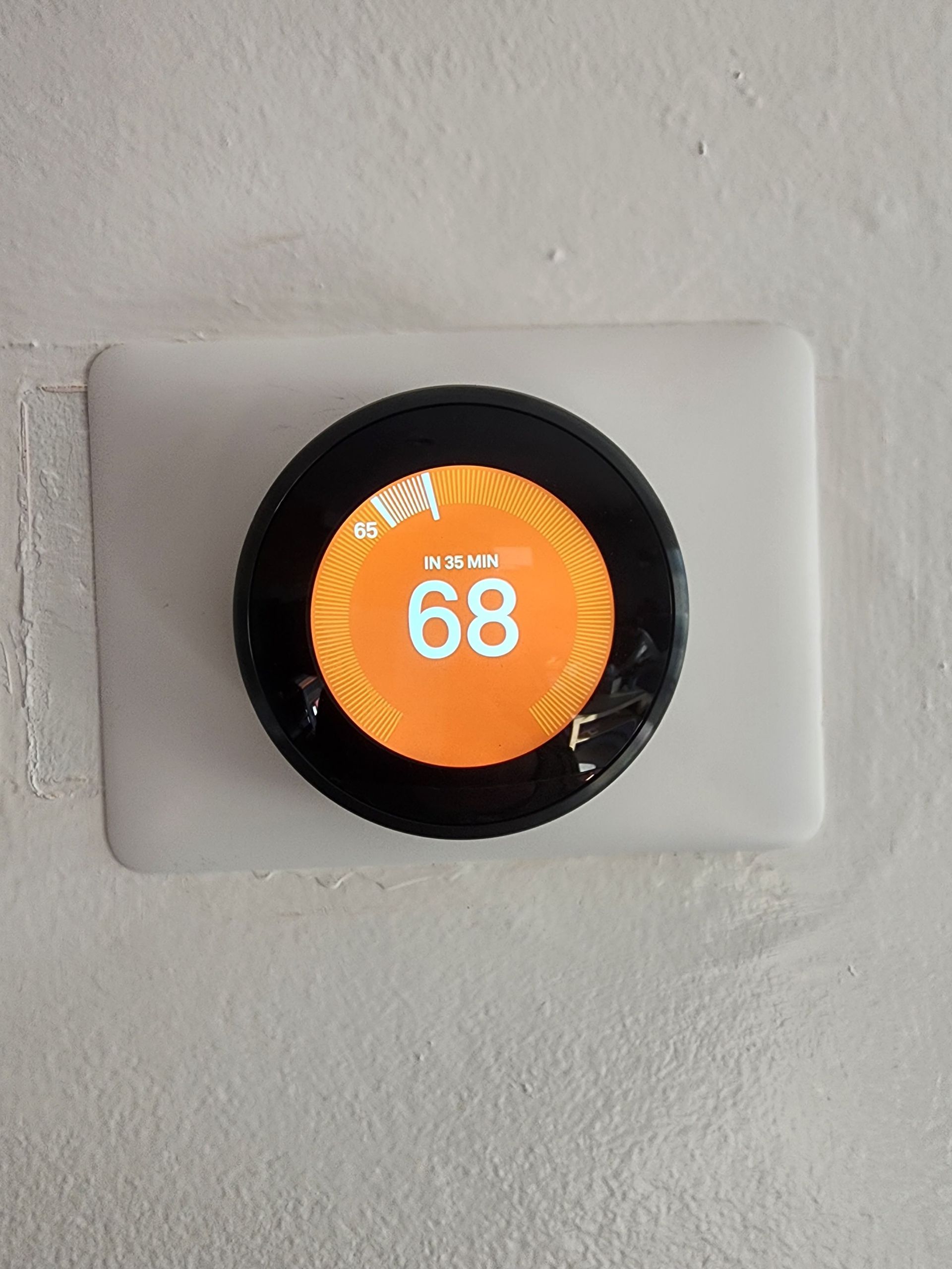 A thermostat is mounted on a wall and the temperature is 68 degrees