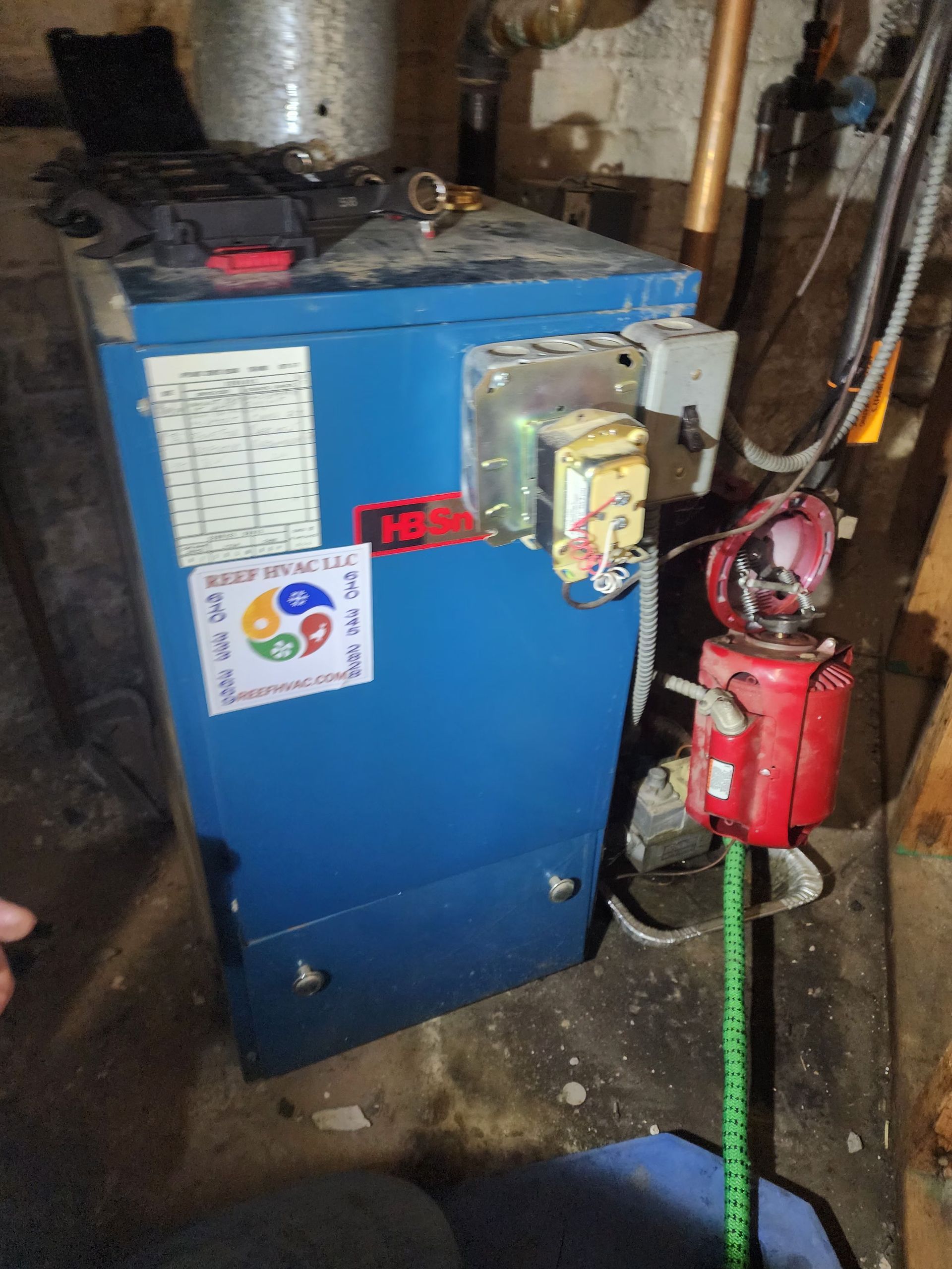 A blue boiler is sitting in a basement next to a measuring tape.