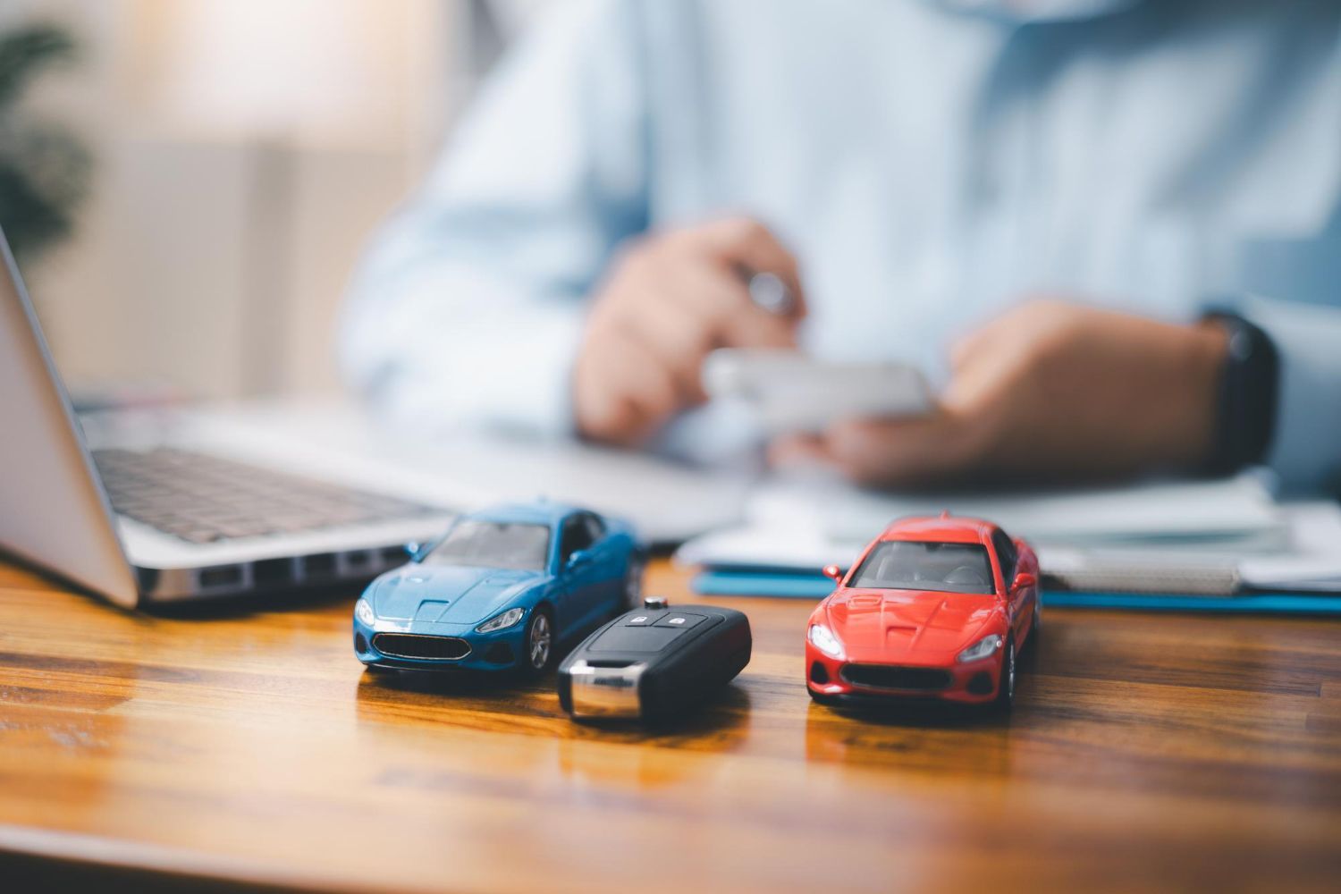 A man is sitting at a desk with three toy cars and a laptop.