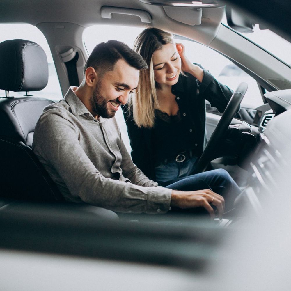 A man and a woman are sitting in a car looking at a laptop.