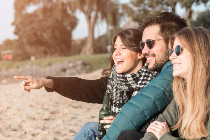 A group of people are sitting on the beach and one of them is pointing at something.