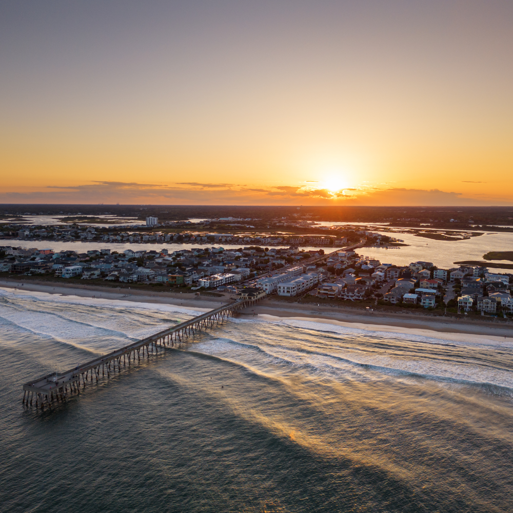 An aerial view of a pier overlooking the ocean at sunset.