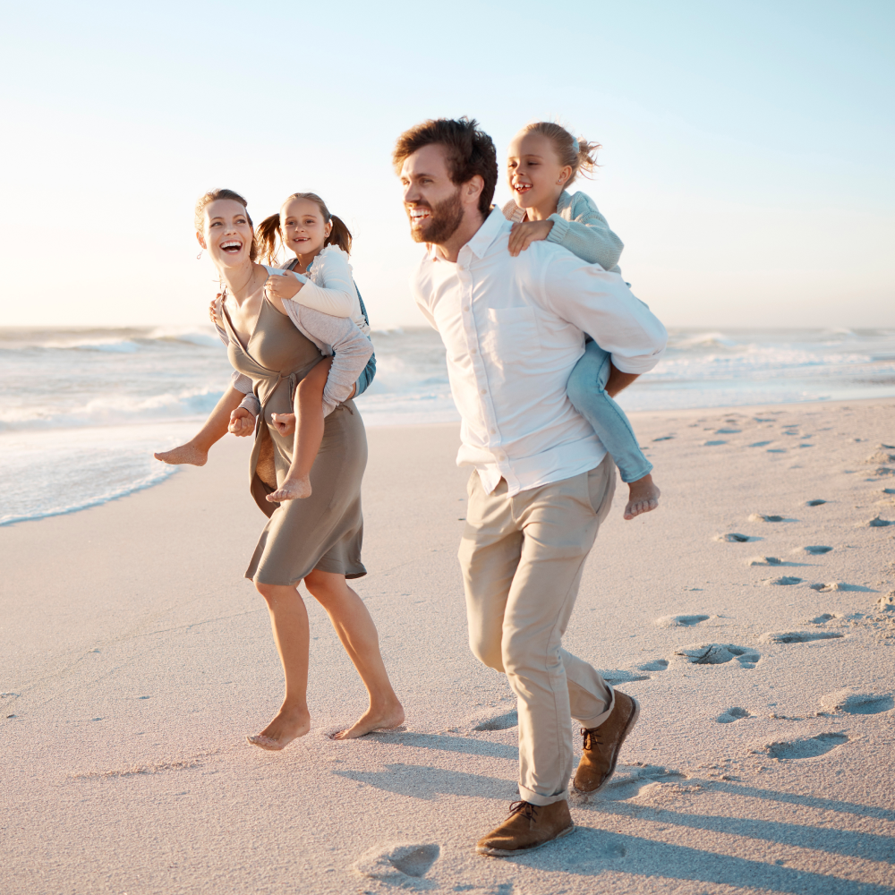 A man is carrying two children on his shoulders on the beach