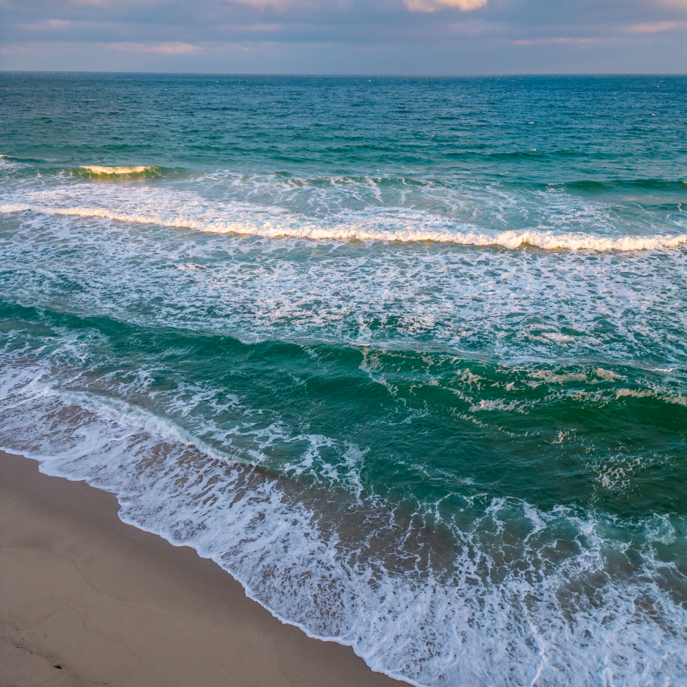 Waves crashing on a sandy beach with a blue sky in the background.