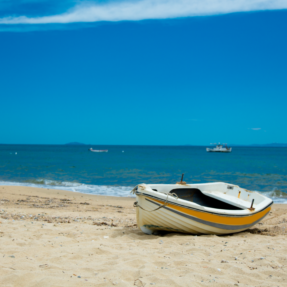 A yellow and white boat sits on a sandy beach near the ocean