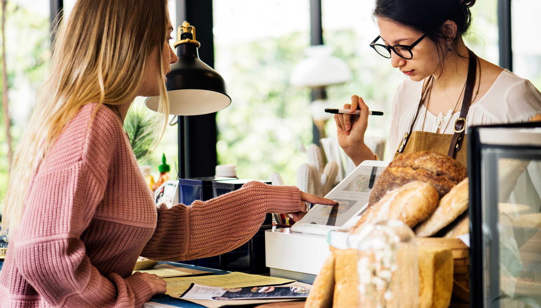 A woman is sitting at a counter in a bakery talking to another woman.