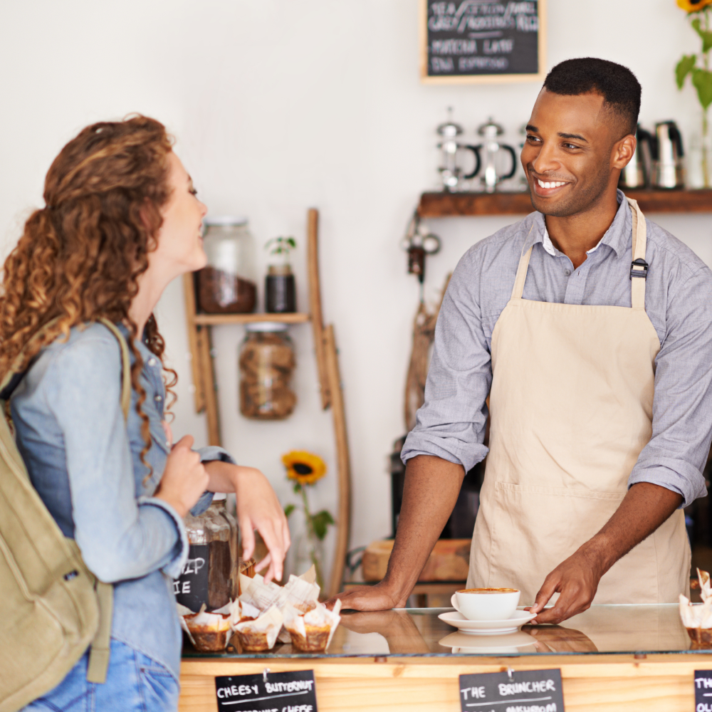 A man in an apron is talking to a woman in a cafe