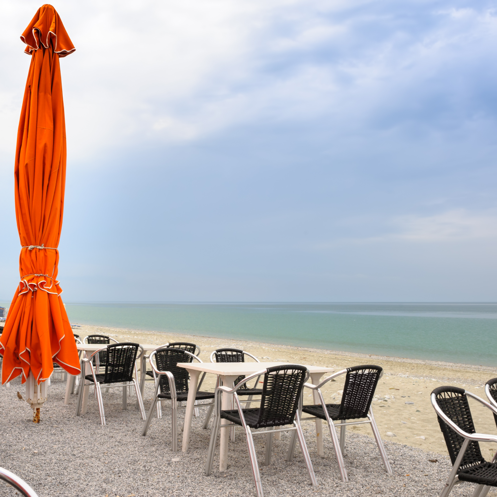 A beach with tables and chairs and an orange umbrella