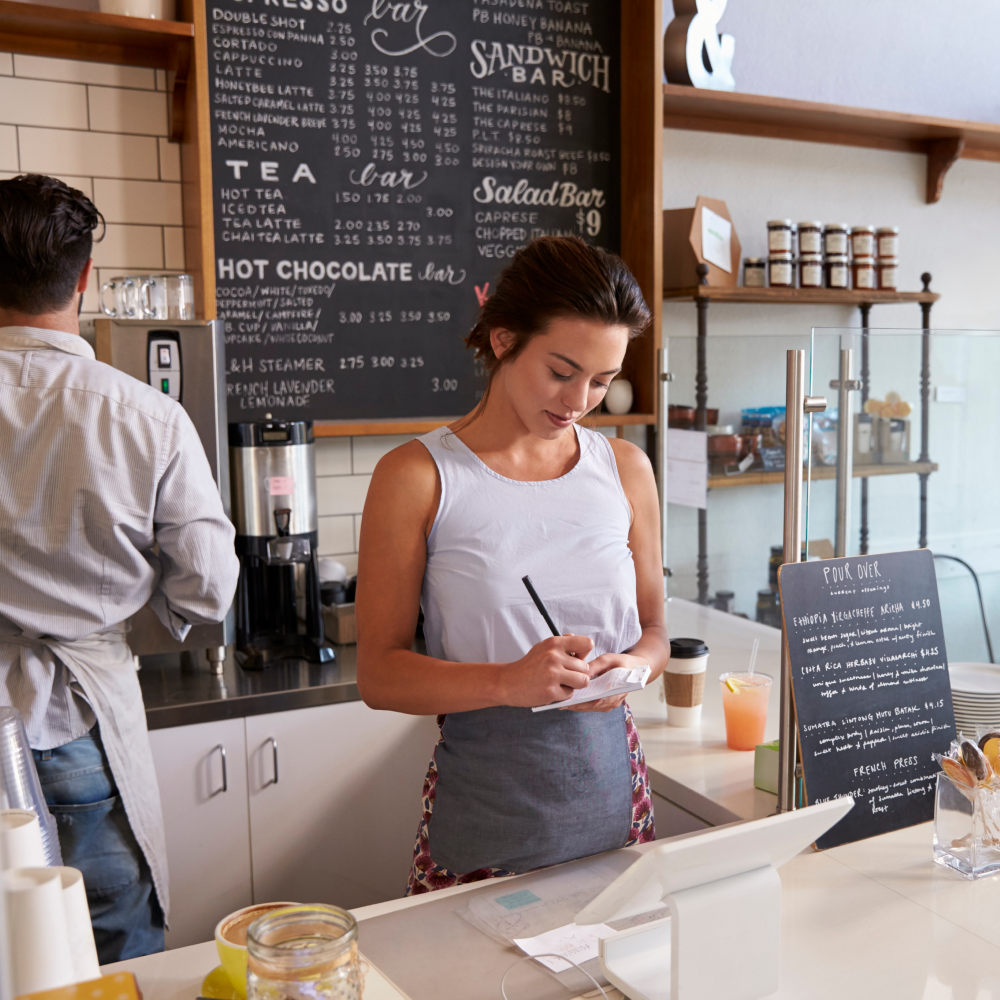 A woman is standing at a counter in front of a menu that says hot chocolate