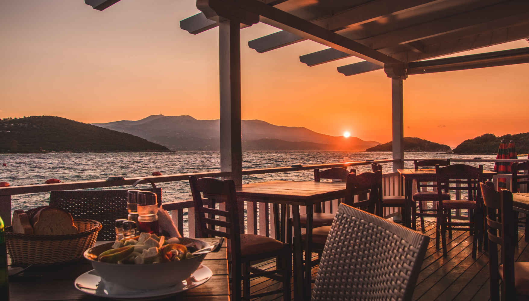 A restaurant with tables and chairs overlooking the ocean at sunset.