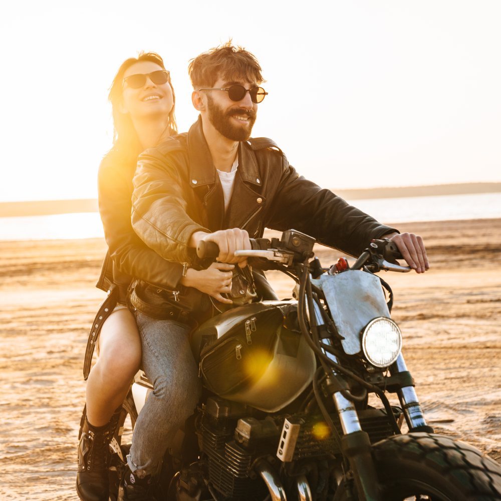 A man and a woman are riding a motorcycle on the beach.