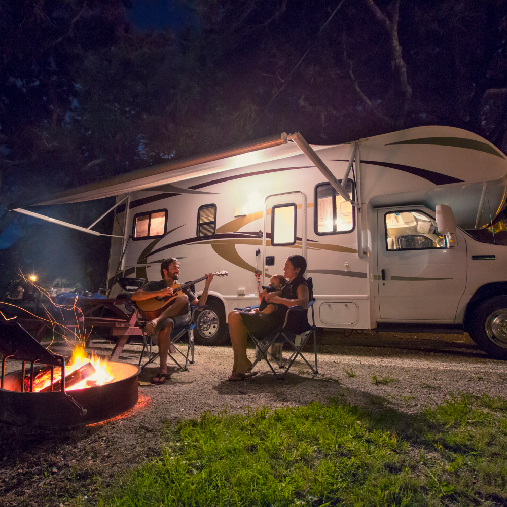 A man is playing a guitar in front of a rv at night.