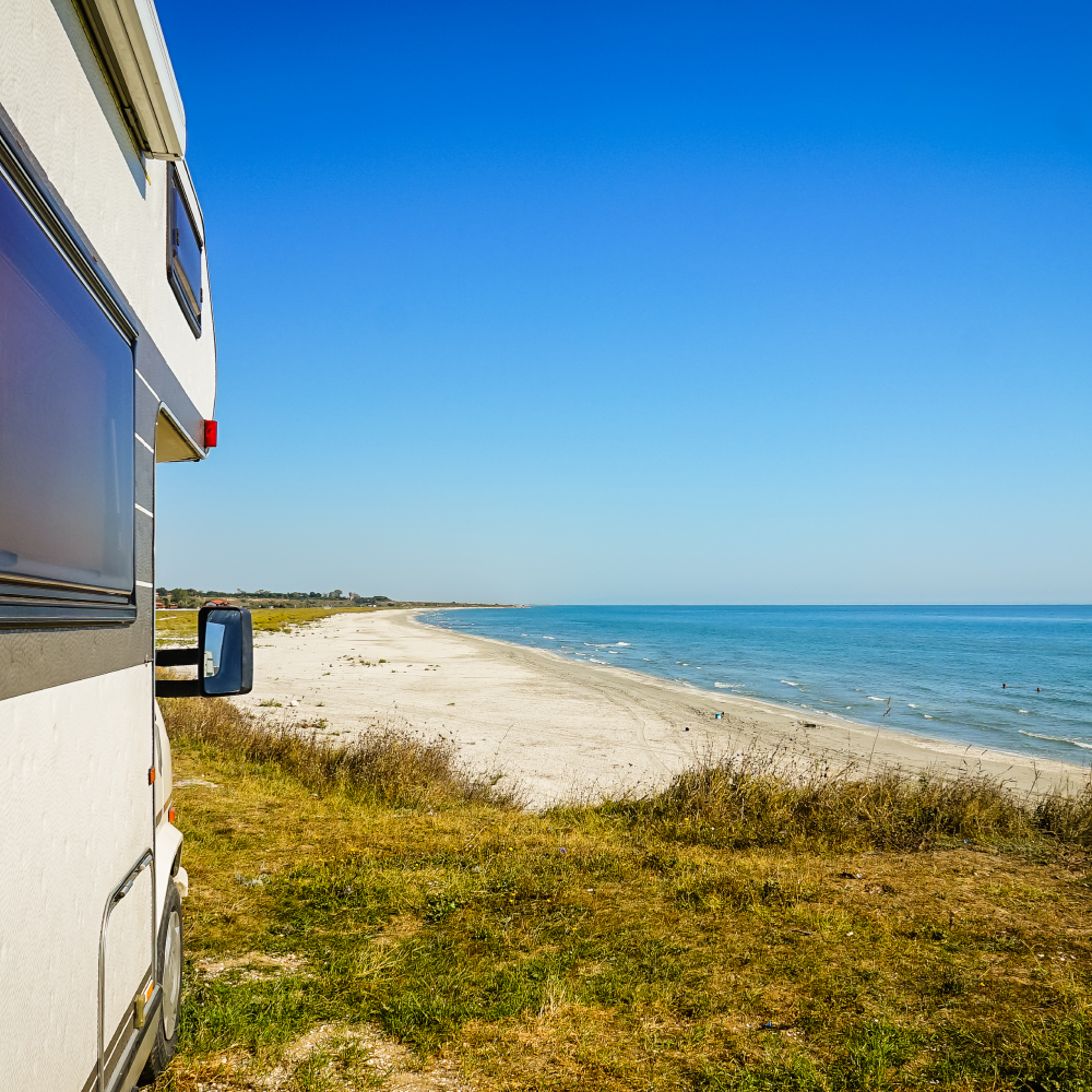A rv is parked on the beach with a view of the ocean.