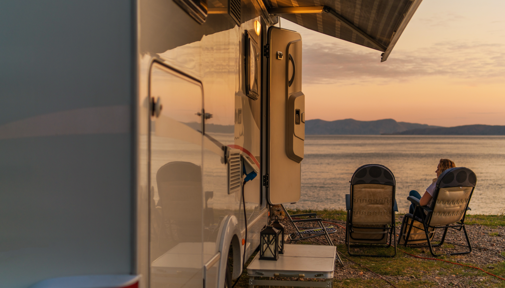 A couple is sitting in chairs on the beach next to a rv.