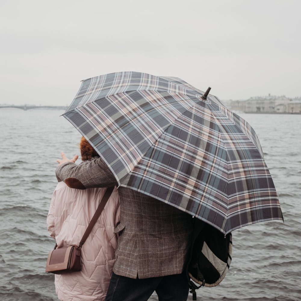 A man and a woman are standing under an umbrella by the water.