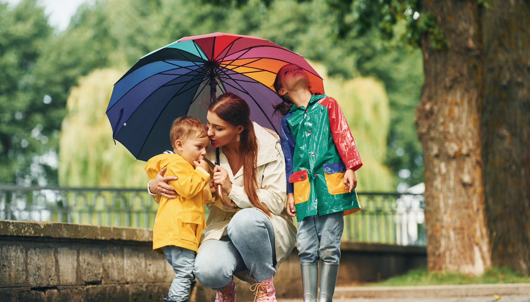 A woman and two children are sitting under an umbrella in the rain.