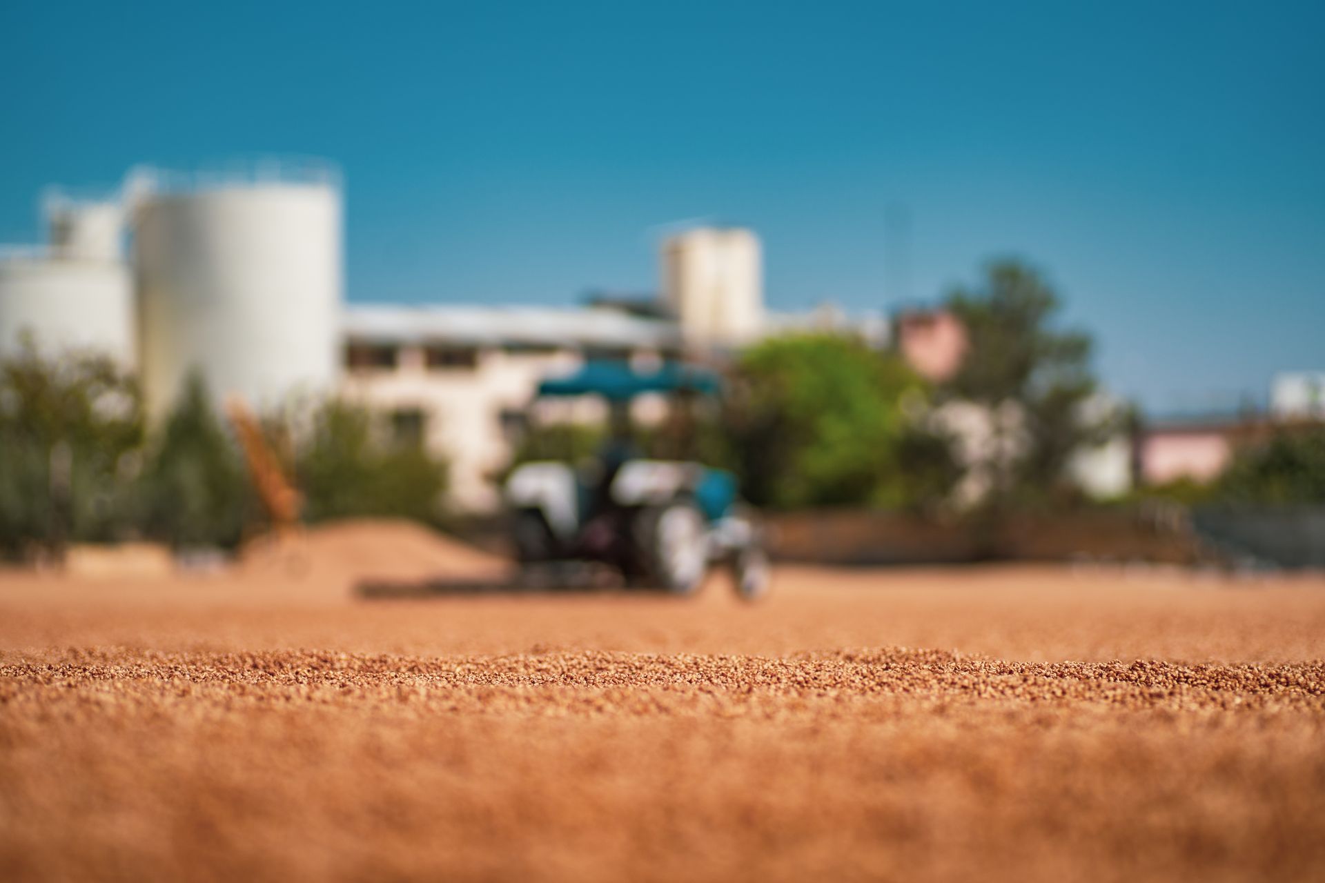 Um trator está arando um campo com um prédio ao fundo.