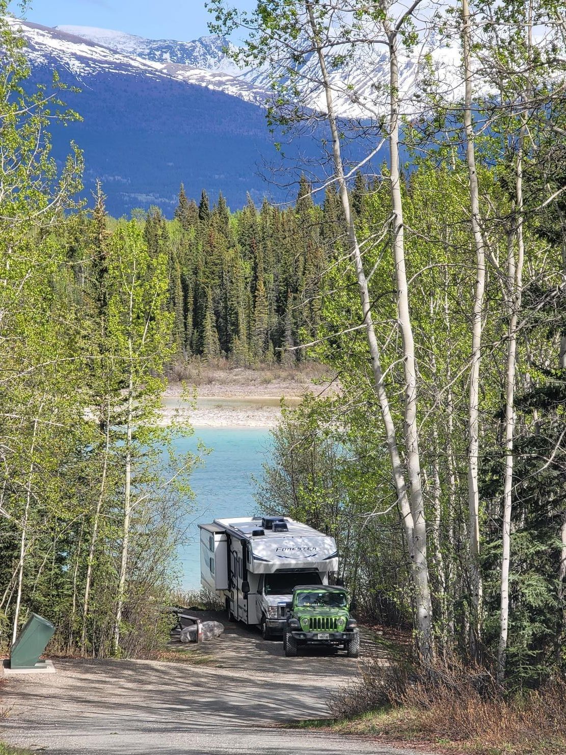 Forest River Forester and Jeep Wrangler at a campsite along the lake at Boya Lake Provincial Park turquoise water and campground in northern British Columbia
