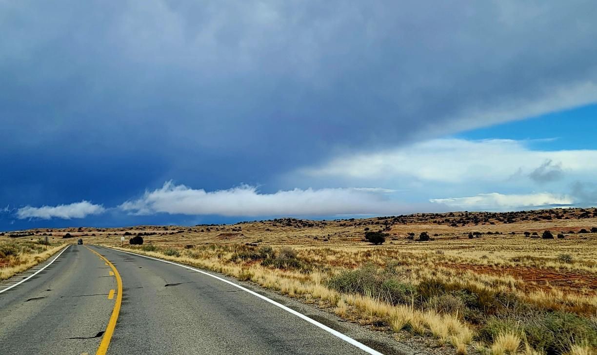 Road through arid landscape under dramatic dark and light storm clouds.