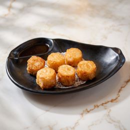 Six golden fried bites on a black oval plate on a marble table