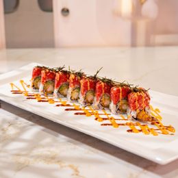 Sushi roll topped with strawberries and drizzled sauce on a white rectangular plate