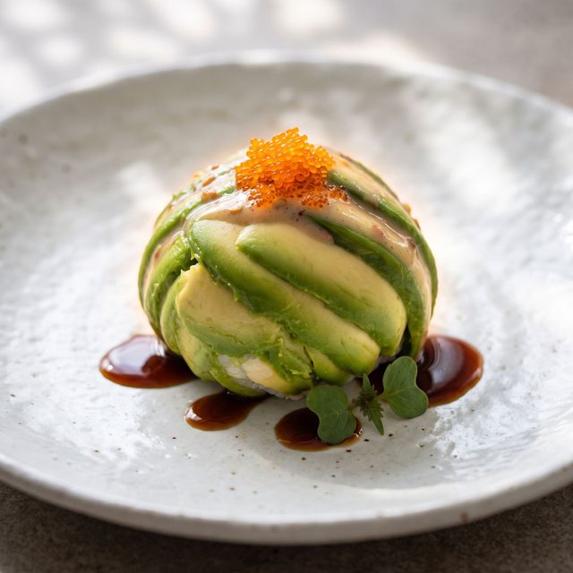 Artfully plated avocado dessert with orange garnish and dark sauce on a white plate