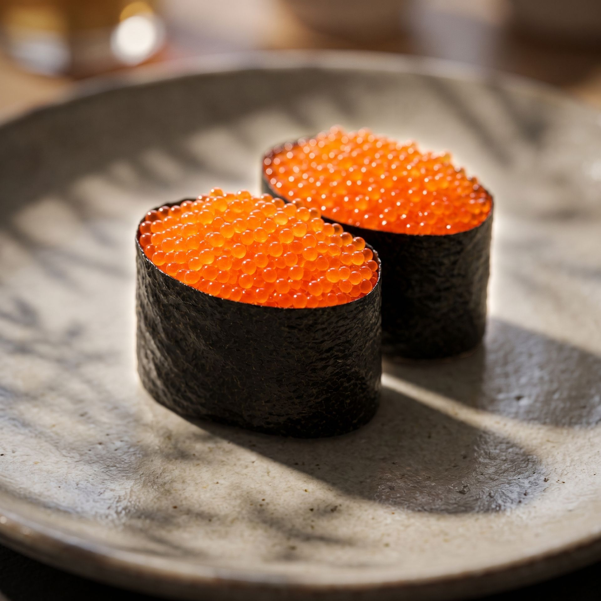 Two salmon roe sushi pieces on a gray ceramic plate