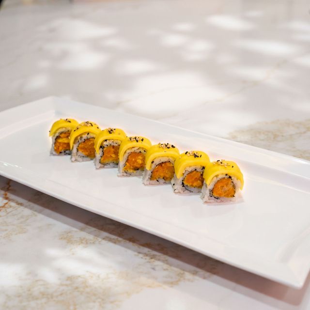 Sushi rolls topped with yellow sauce on a long white platter