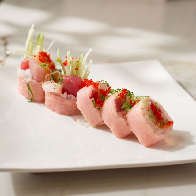 Slices of pink sashimi garnished with green onion and red roe on a white plate