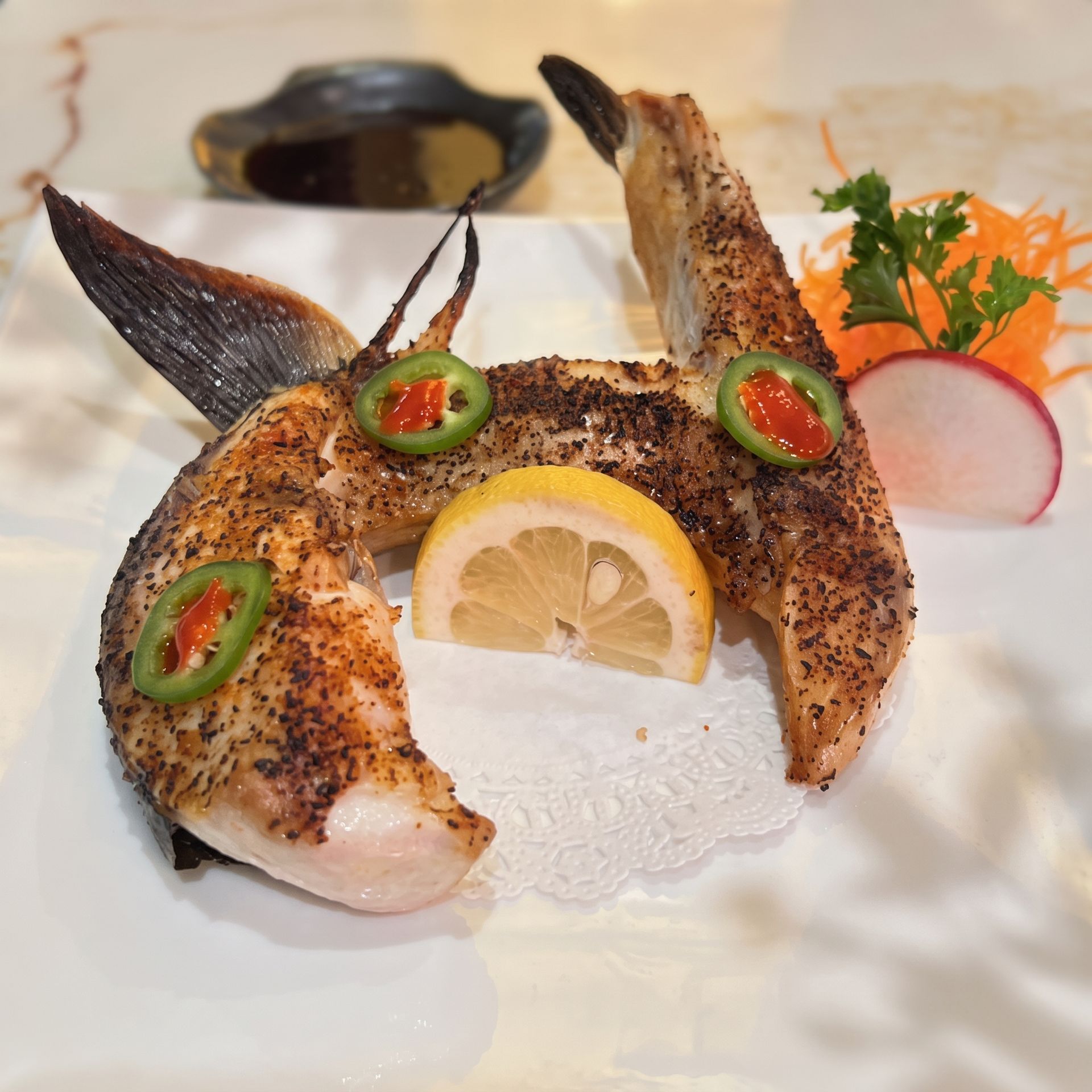 Plated grilled fish with lemon slice and jalapeño garnishes, served with radish and herbs