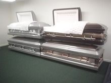 Stacked coffin-shaped objects on a table in a room, with framed documents behind them.