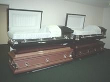 Three open caskets displayed side by side in a room, including white and brown finishes.