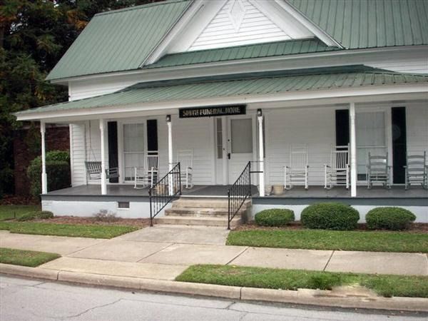 Front entrance of a white historic building with green metal roof, porch, steps, and ramp accessible entrance
