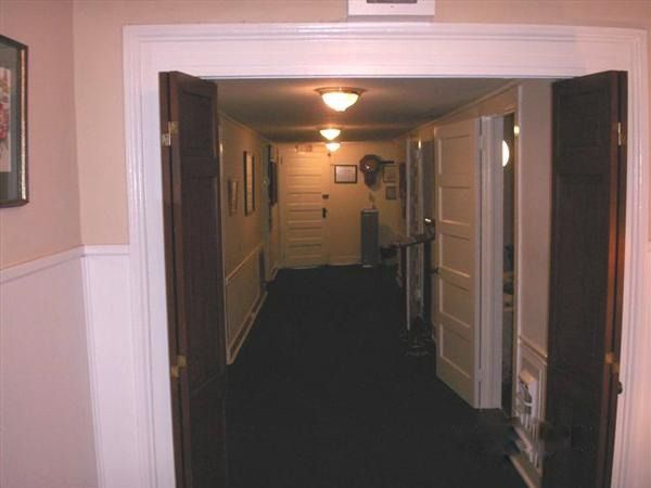 Empty hallway with open doors, white trim, and dark carpet under warm ceiling lights