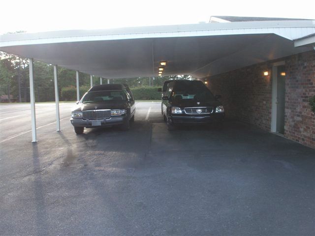 Two dark SUVs parked under a covered driveway beside a brick building.