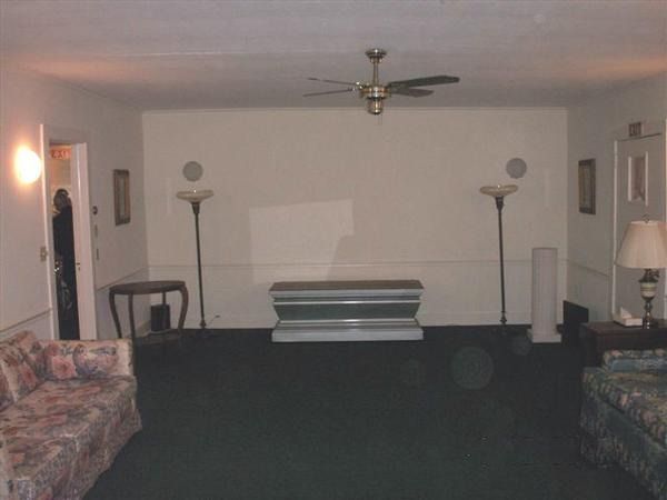 Living room with a central coffin or casket, flanked by floor lamps and sofas.