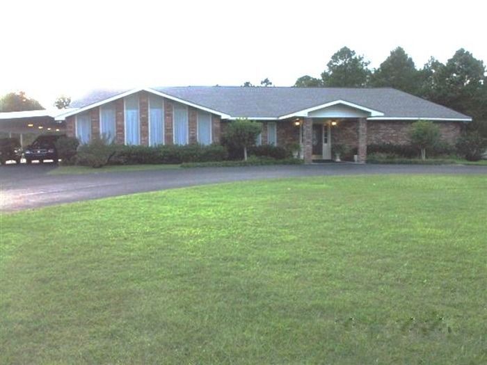 Single-story brick house with a large green lawn and driveway in front