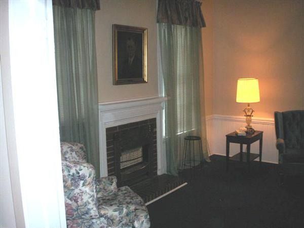Living room with fireplace, floral chair, curtained windows, and a lit lamp on a small table.