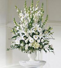 White floral arrangement in a silver urn on a pedestal, with tall white blooms and greenery