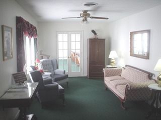 Bright living room with green carpet, sofa, armchairs, lamp, and French doors to a balcony