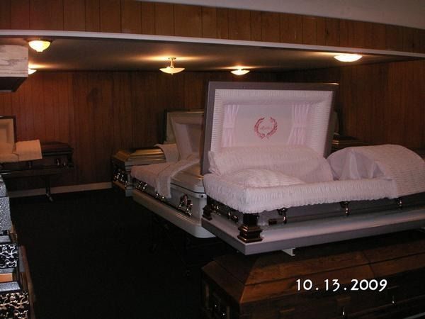 Flower-covered casket in a dim wood-paneled funeral viewing room