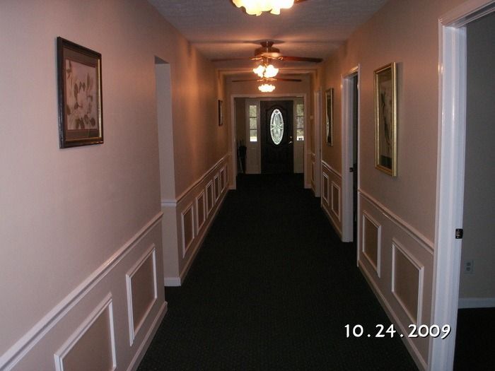 Long hotel hallway with beige walls, dark carpet, framed art, and a door at the end.