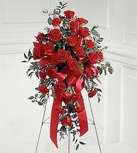 Red rose floral arrangement on a stand with flowing ribbons against a white wall