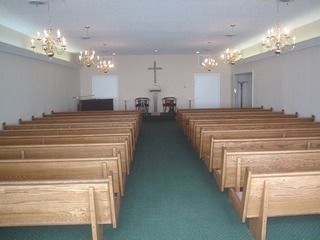 Empty church interior with wooden pews, green carpet, and a cross at the altar