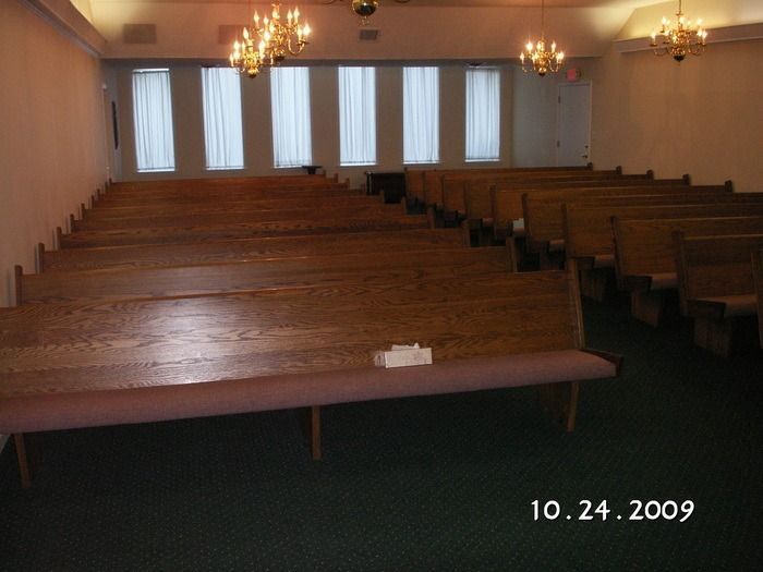 Empty church sanctuary with wooden pews, chandeliers, and tall windows