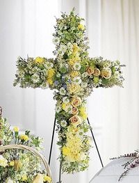 Floral cross-shaped arrangement with white, yellow, and green flowers on a stand