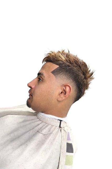 A side profile of a person wearing a barber cape, showcasing a textured, light brown haircut with a sharp skin fade.