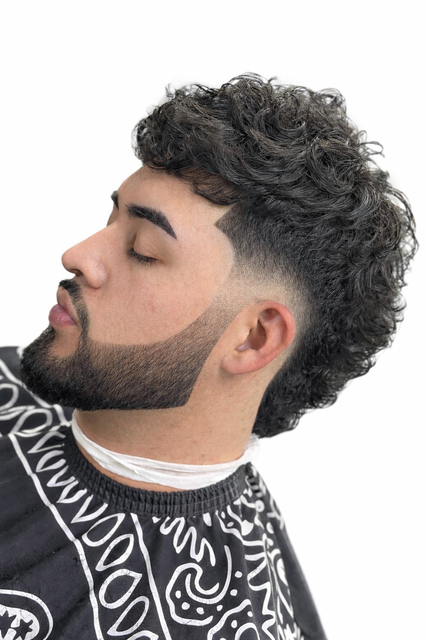 A person with a curly-haired fade haircut and groomed beard, captured in profile against a plain white background.