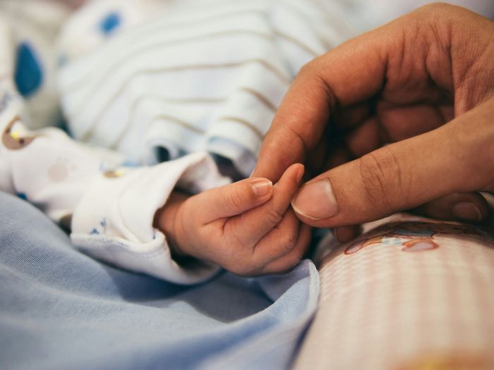 A baby and parent holding hands, only the hands are shown.